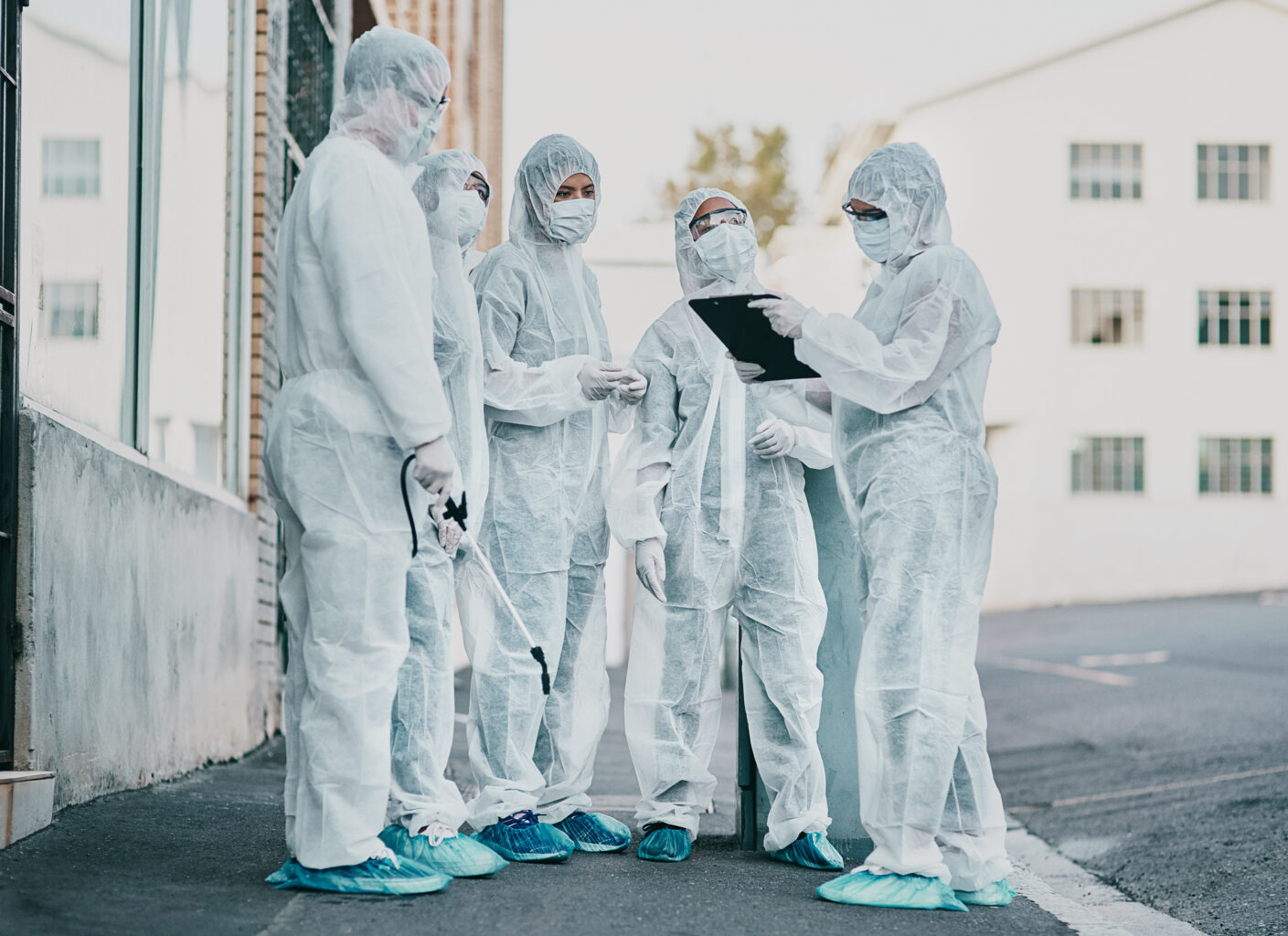 Covid, pandemic and healthcare team wearing protective PPE to prevent virus spread at a quarantine site. First responders wearing hazmat suits while discussing plan for cleaning and disinfecting.